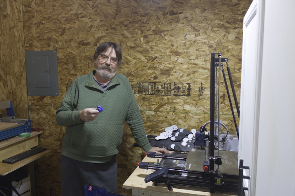 Terry Palchuk, holding up a 3D item and leaning next to a 3D printer at the 100 Mile and Area's Mens Shed at the 108 Mile Ranch on Dec. 6 (Misha Mustaqeem photo - 100 Mile Free Press) 