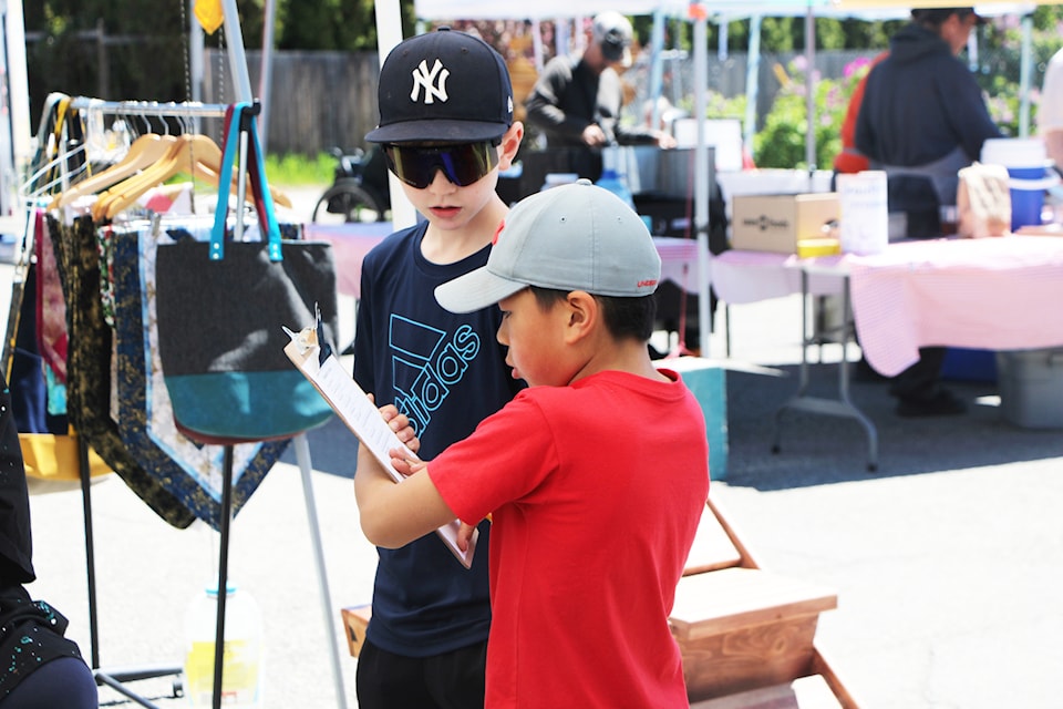 100 Mile Elementary School students Ben Nash and Ben Ma write down the answers of a vendor at the South Cariboo Farmers Market as they complete survey last week. (Patrick Davies photo - 100 Mile Free Press)