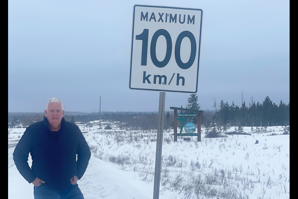 Thompson Nicola Regional District Director Jim Smith poses for a photo with the speed limit sign leading into 70 Mile House. Smith wants to see the speed reduced to 80 km/hr through 70 Mile House. (Photo submitted)