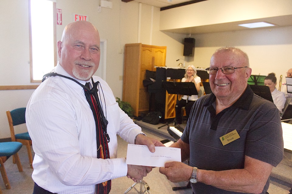 Eric Grummish hands a cheque to the South Cariboo Health Foundation's Bruce Madhu during the 100 Mile Community Band's season-end concert, held at the 100 Mile United Church on June 7. In the background is Rose Wall, who played clarinet. (Misha Mustaqeem photo - simplymastery)