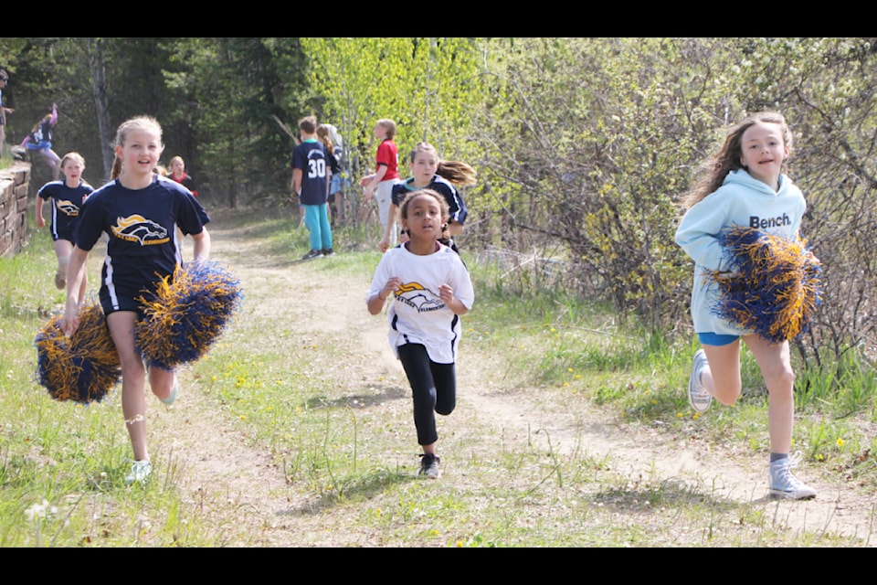 Horse Lake Elementary School Grade 6 students Ariella Norfolk (left) and Mackenzie Thibeault (right) run alongside and cheer on Layla Elliston, Grade 3, as she competes in the 2025 South End Cross Country Run. (Patrick Davies photo - simplymastery)
