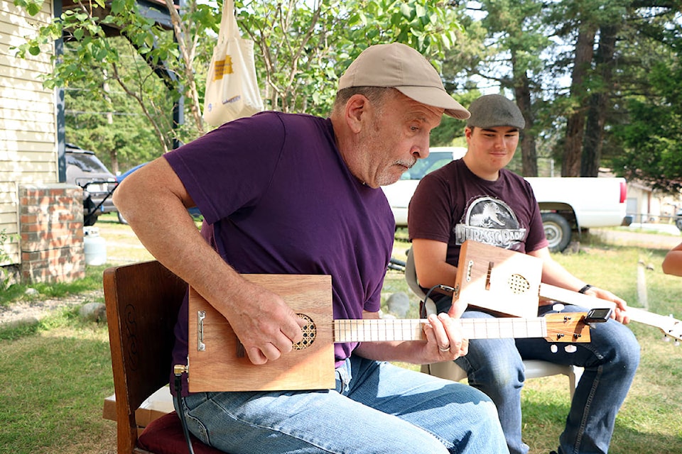 Peter Thorne demonstrates a simple tune while Evan Kalmokoff watches with his handmade cigar box guitar. (Patrick Davies photo- 100 Mile Free Press)