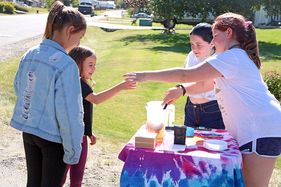 A pair of sisters grab two cups of lemonade from Payton Meindi (far left) while Kaitlyn Querques watches. Meindi and Querques created their makeshift lemonade stand as something to do that wasn’t sitting around their house on their phones as said they served lemonade to at least 50 people along Cariboo Trail. (Patrick Davies photo- 100 Mile Free Press)