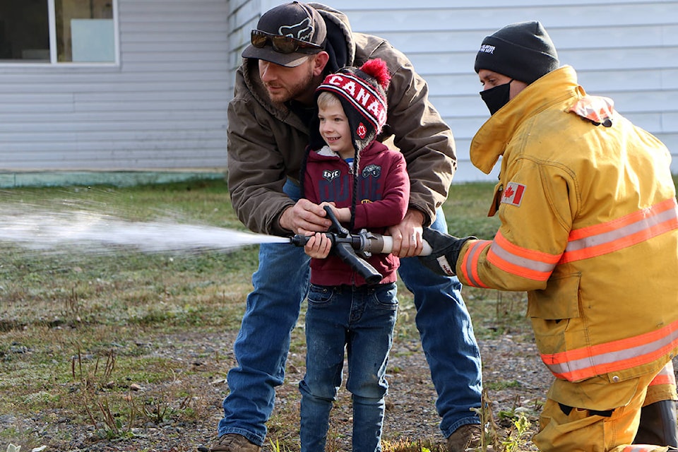 Kaiden Davidson (centre) smiles as he uses a fire hose with the help of his dad Dustin Davidson and Forest Grove firefighter Andrew Grey. (Patrick Davies photo - 100 Mile Free Press)