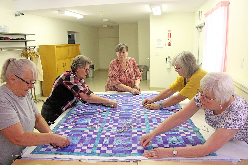 Members of the Cariboo Calico Quilters guild work together to pin pieces of fabric in place as they construct a comfort quilt at the Creekside Senior’s Centre. (Patrick Davies photo - 100 Mile Free Press)