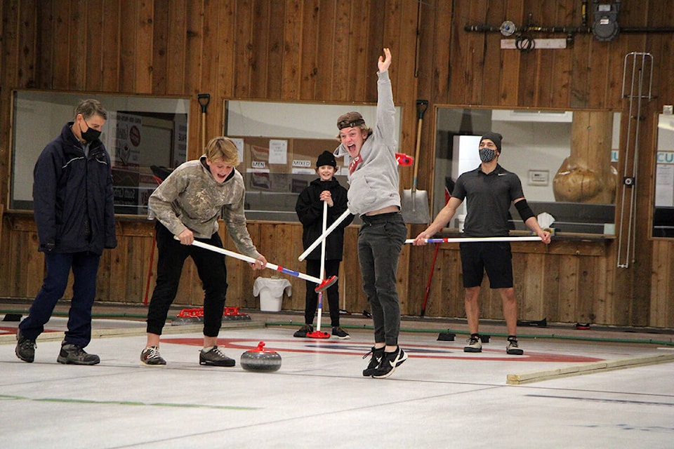 As 100 Mile House Curling Club president Gord Smith comes in to officiate (front left) Gibson Fast and Mason Pincott celebrate a successful throw while classmate Reichert Sanford (back) and teacher Kameron Taylor watch. (Patrick Davies photo - 100 Mile Free Press)