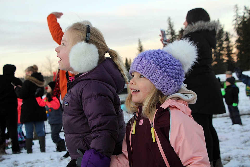 Evelyn Lethwaite and Amelia Law watch with wonder as Santa Claus’ plane circles the runway at the 100 Mile House Airport last week. (Patrick Davies photo - 100 Mile Free Press)