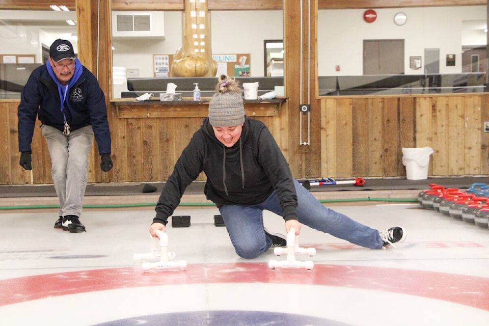 Richard Minato watches as the Free Press’ Melissa Smalley tries her hand at curling at the 100 Mile House Curling Club. (Patrick Davies photo - 100 Mile Free Press)