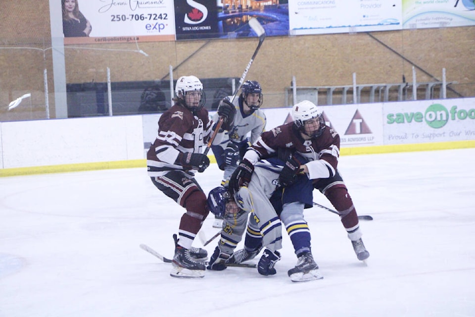 The Revelstoke Grizzlies’ Kaleb West (front left) works to keep 100 Mile House Wrangler Chase Sitarski tied up with the help of Spencer Macdonald while Solomon Oldham (back) skates for the puck. (Patrick Davies photo - 100 Mile Free Press)