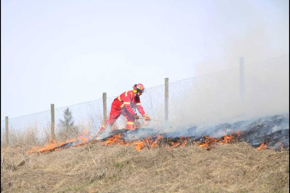 A firefighter works on extinguishing a grass fire behind the South Cariboo Rec Centre on Wrangler Way Tuesday. (Patrick Davies photo - 100 Mile Free Press).
