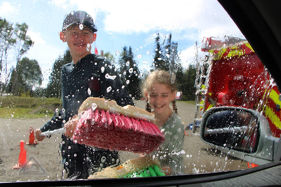 Landen Warburton laughs as he cleans the window of a car with Emily Smith at the first annual Neil Hodge Memorial Car Wash in Forest Grove. (Patrick Davies photo - 100 Mile Free Press)