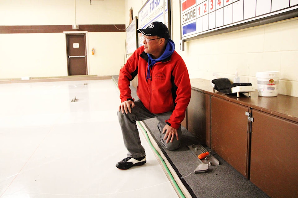 Richard Minato makes sure a piece of string that shows the middle of a lane of ice is straight last week while putting in a new sheet of ice. (Patrick Davies photo - 100 Mile Free Press)