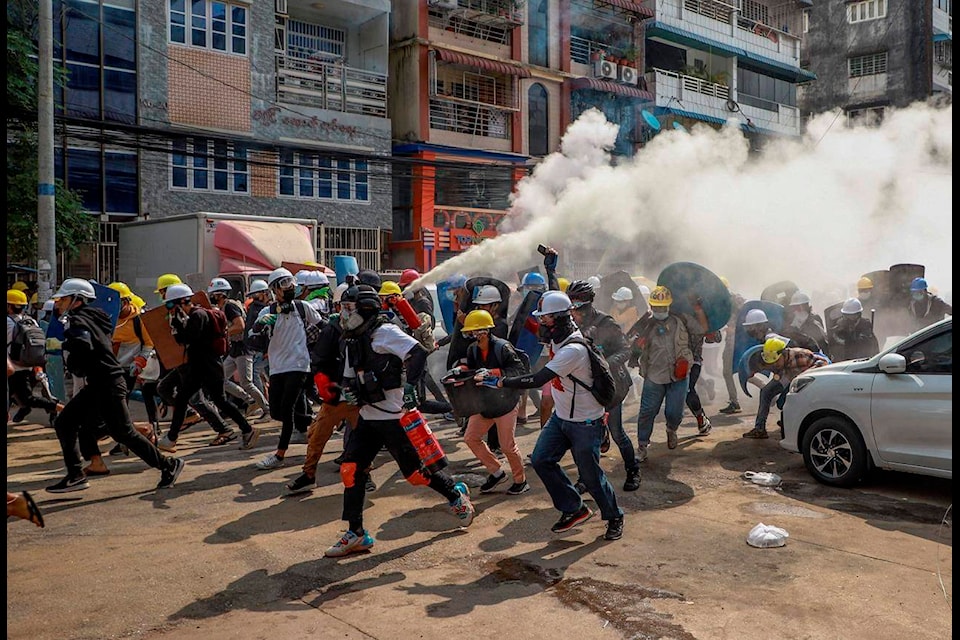 FILE - In this March 3, 2021, file photo, anti-coup protesters run as one of them discharges a fire extinguisher to counter the impact of tear gas fired by riot policemen in Yangon, Myanmar. The escalation of violence in Myanmar as authorities crack down on protests against the Feb. 1 coup is adding to pressure for more sanctions against the junta, as countries struggle over how to best confront military leaders inured to global condemnation. (AP Photo/File)