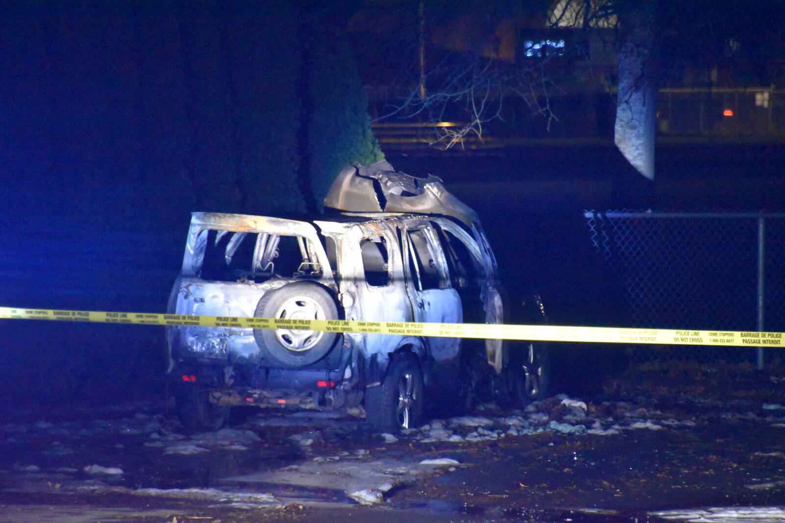 A burned out SUV behind police tape after 6:45 p.m. on Dec. 13, 2022 at the Tzeachten sports field on Bailey Road in Chilliwack less than an hour after a homicide at a residence on Windsor Street. (Curtis Kreklau photo)