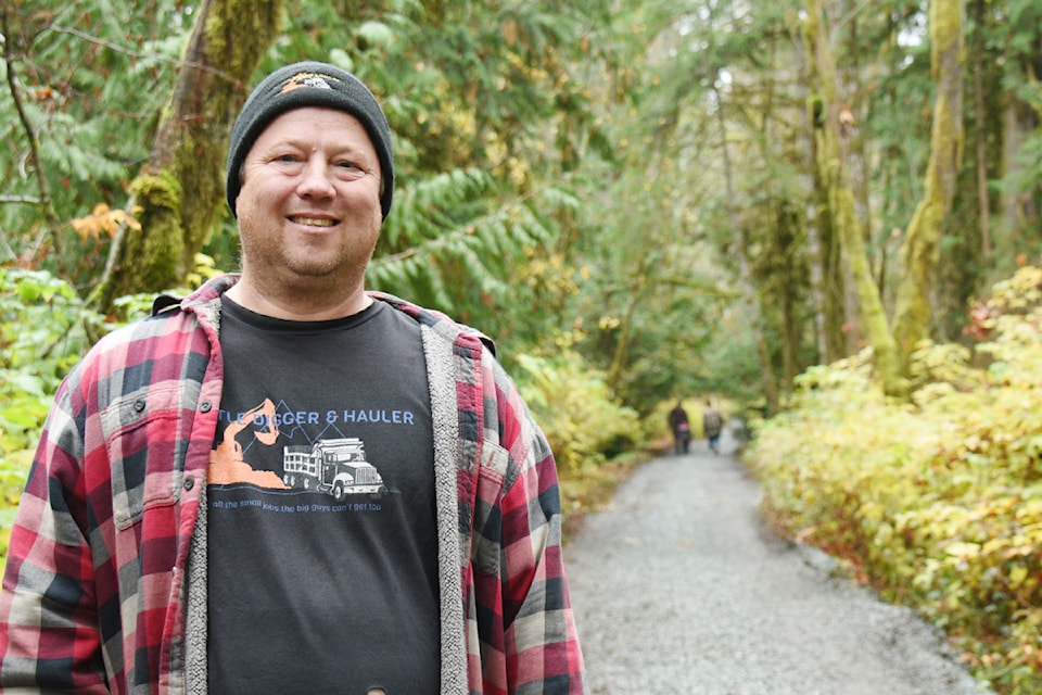 Jamie Donovan of AV Little Digger and Hauler stands beside the Rogers Creek trail that he restored on behalf of a film crew that used it during rainy weather in October. Rick Hebert and his wife terry walk with their grandson in the background. 