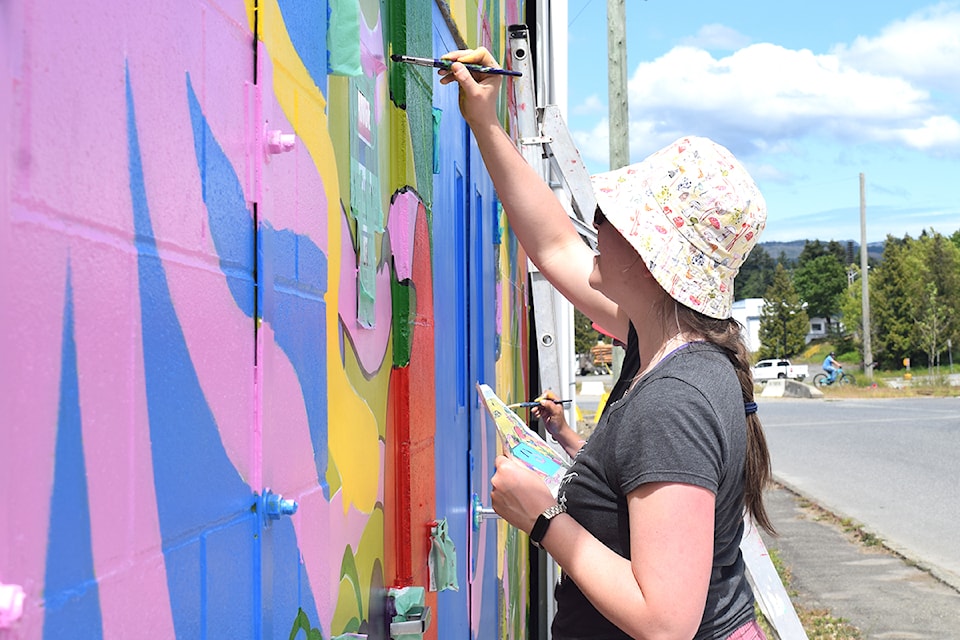 Josée Baillargeon paints a mural outside of The Dock+ on Saturday, May 24, 2025 at Tyee Landing. (ELENA RARDON/ Alberni Valley News)