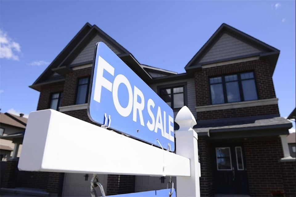 A 'for sale' sign sits on a lawn of a single-family home.