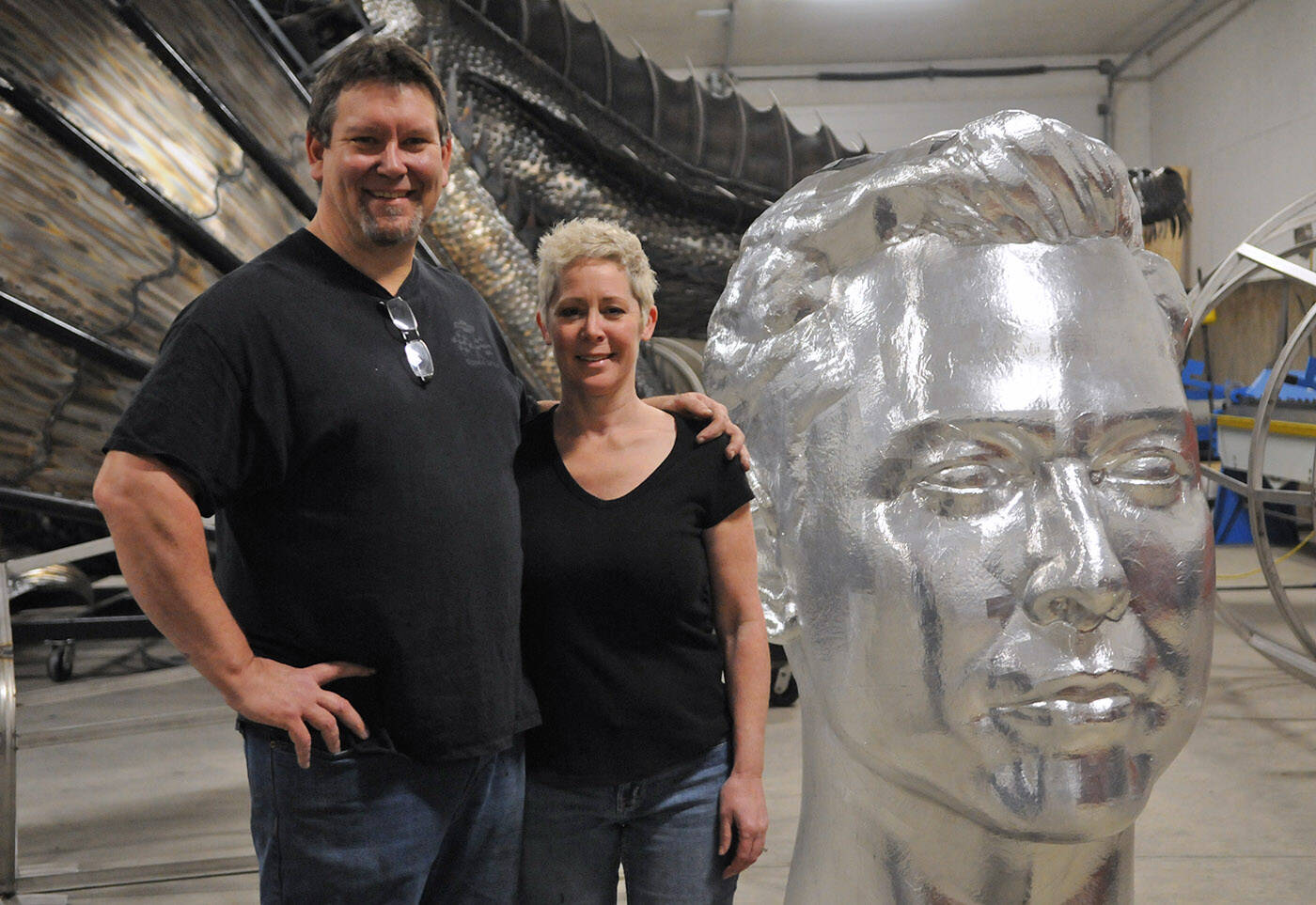 Kevin and Michelle Stone stand beside a giant Elon Musk head at their workshop on Tuesday, Jan. 18, 2022. (Jenna Hauck/ Chilliwack Progress)