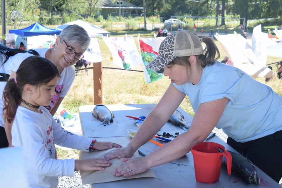 Kristin Kerr-Donahue helps Lennox Alexander stamp a fish at Beaver Creek Community Hall for Alberni Valley Rivers Day. (ELENA RARDON / ALBERNI VALLEY NEWS)