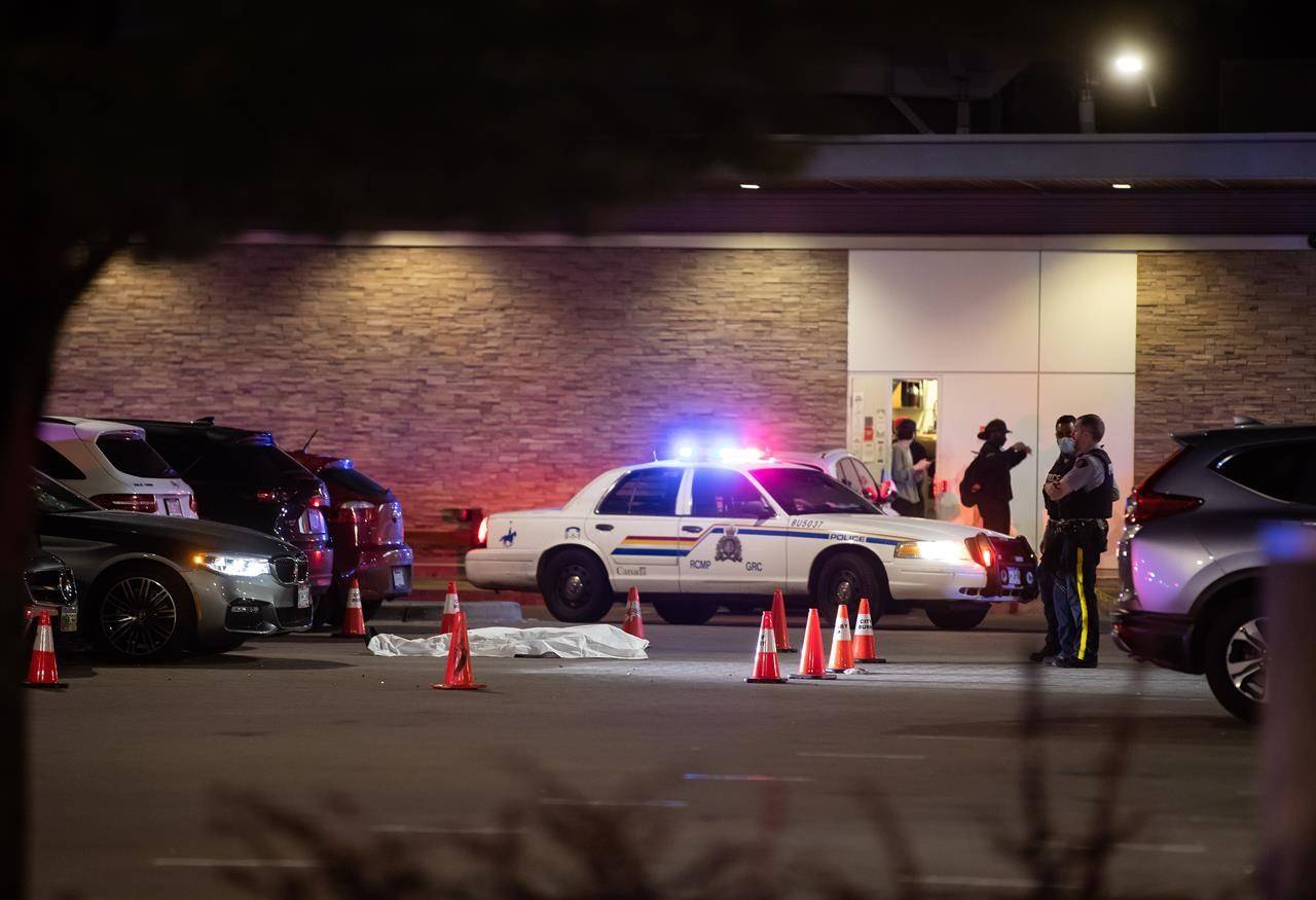 RCMP officers stand near a body covered with a tarp in the parking lot of a shopping complex after Brothers Keepers member Jaskeert Kalkat, 23, was killed during a shooting in Burnaby on May 13, 2021. THE CANADIAN PRESS/Darryl Dyck