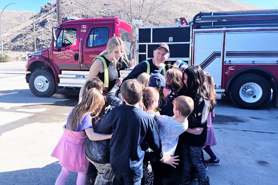 Cache Creek Junior Firefighter Emma Gross and Fire Chief Tom Moe get a group hug from Mrs. Pigeon’s Cache Creek Elementary Grade 2/3 class on a recent visit, where the students had a very special surprise for the pair. (Photo credit: Nicole Pigeon)