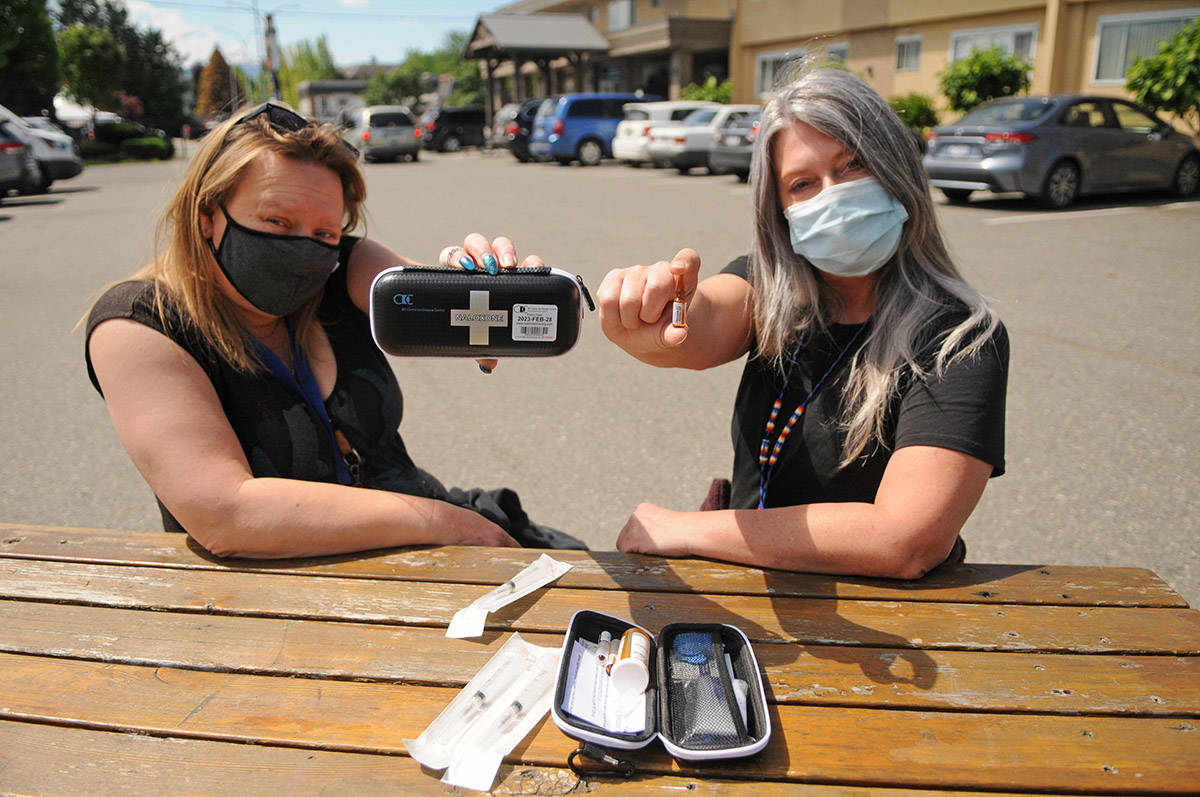 Jodi Higgs (right) holds a vial of naloxone and Christine Christensen holds a kit in the parking lot of the Pacific Community Resources Society in Chilliwack on Thursday, May 20, 2021. The society is offering a number of upcoming events, workshops and videos to help educate friends and family members who have loved ones that are drug users. (Jenna Hauck/ Chilliwack Progress)