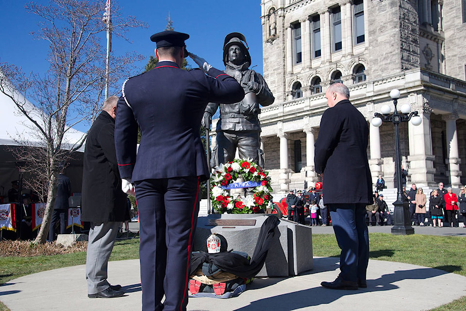 A firefighter salutes the commemorative statue behind the BC Legislature during the BC Fallen Fire Fighters’ memorial, with B.C. Professional Fire Fighters Association executive director, Gord Ditchburn, on the left and B.C. Premier John Horgan on the right (Nicole Crescenzi/News Staff)