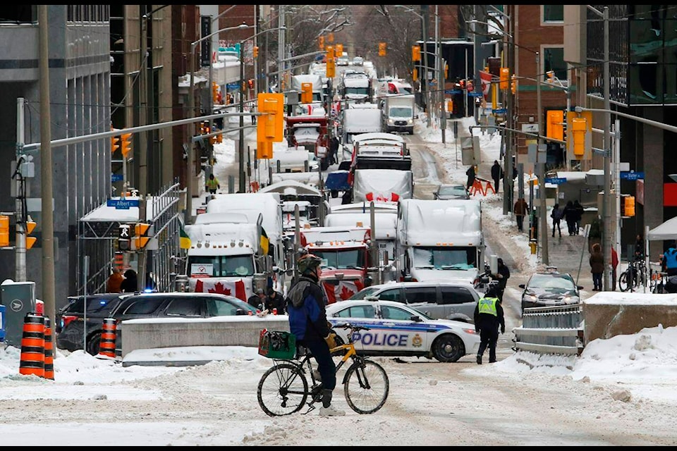 A cyclist stops in front of trucks blocked on Metcalfe Street as a rally against COVID-19 restrictions, which began as a cross-country convoy protesting a federal vaccine mandate for truckers, continues in Ottawa, on Friday, February 4, 2022. THE CANADIAN PRESS/ Patrick Doyle