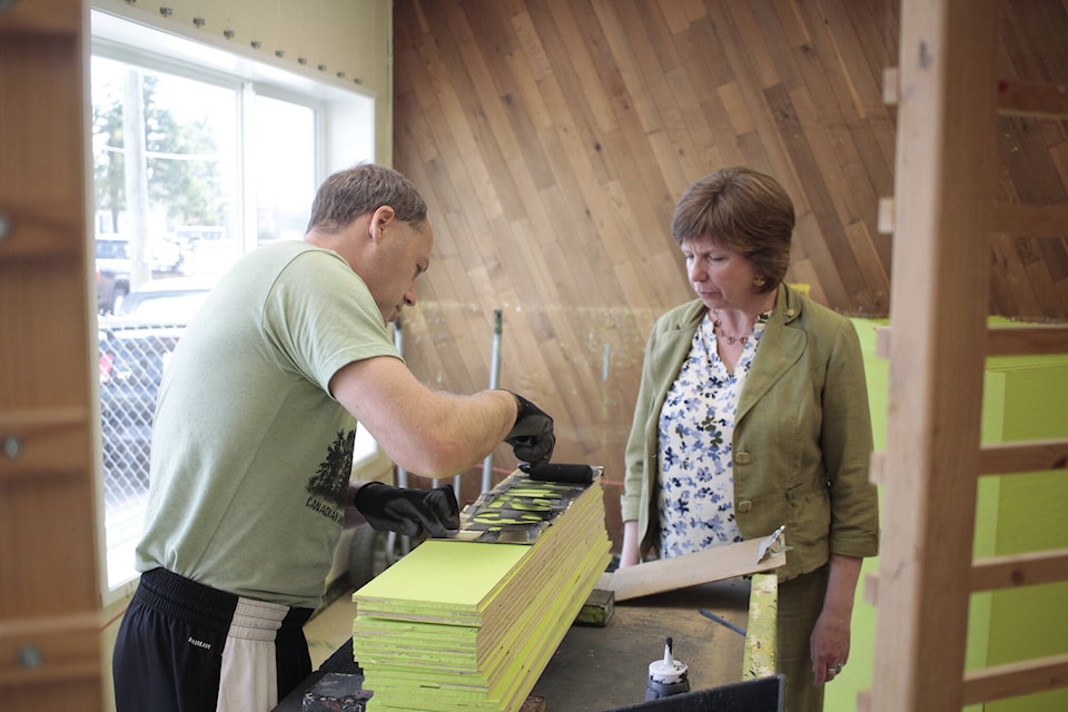 Ken Sloan shows Minister Sheila Malcolmson how to paint log boom boards at Skyline Productions, which is part of Rivercity Inclusion. Photo by Marc Kitteringham/Campbell River Mirror