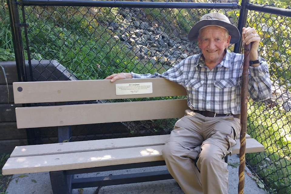Art "The Happy Hiker" Langkeek sitting on a bench named in his honour at the top of the stairs at the Sylvan Drive trailhead near Mt. Thom Drive.