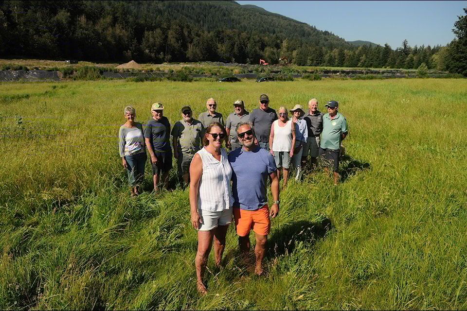 Columbia Valley residents, including D'Arcy Henderson and Jason Vasilash, stand in a field next to the Iverson Road property with the piles of waste behind them, on Friday, July 12, 2024. 