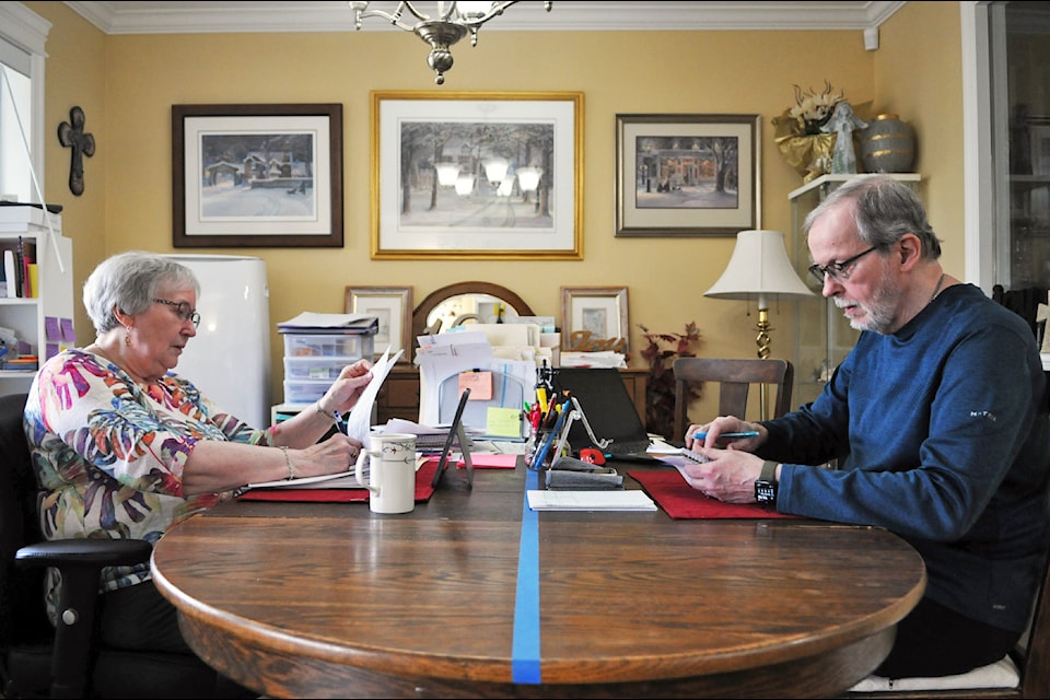 A line of blue tape divides Norm and Diane Melanson's dining-room table in two where, on one side, she fills out ICBC paperwork while he works on his brain exercises. The couple is pictured in their Chilliwack home on April 10, 2025.