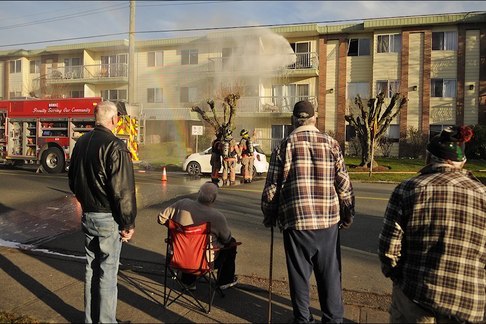 Water sprays out of an apartment unit as a firefighter battles a blaze from inside a complex on Victoria Avenue in Chilliwack on Thursday, Jan. 23, 2025.