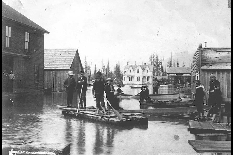 Boys on homemade rafts and men in canoes on Mill Street during the flood of 1894. The photo was taken at the corner of Wellington looking north on Mill Street. Two houses in the background are the residences of W.A. Rose and G. Wilkinson, Victoria Ave. West. Benjamin Southwell Bradshaw sitting in canoe. Two of five boys on raft include Roy Chadsey and Alex Chadsey. Norm McGillivray visible on right with dog. Don McGillivray standing behind Norm. (Photograph courtesy of the Chilliwack Museum and Archives 682).