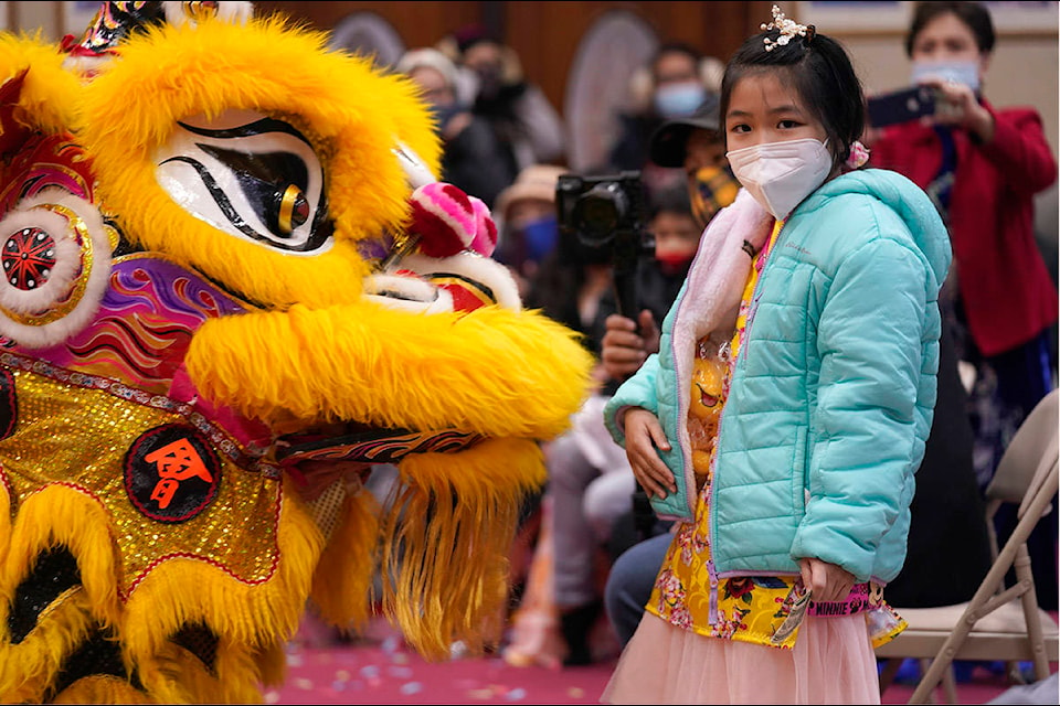 Wearing a mask to prevent the spread of COVID-19, Anna Lee, 9, stands next to lion dancers during a Lunar New Year celebration at Dao Quang Temple on Thursday, Feb. 11, 2021, in Garland, Texas. (AP Photo/LM Otero)