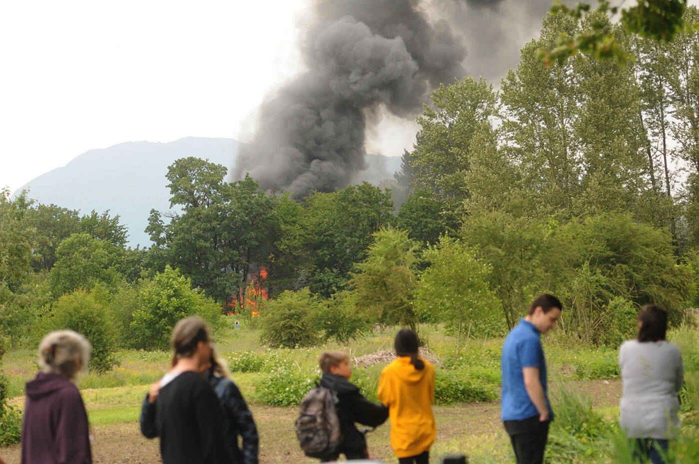 An RV burns on Skwali reserve as people watch from the dike near the west end of Marshall Avenue on Wednesday, June 15, 2022. (Jenna Hauck/ Chilliwack Progress)