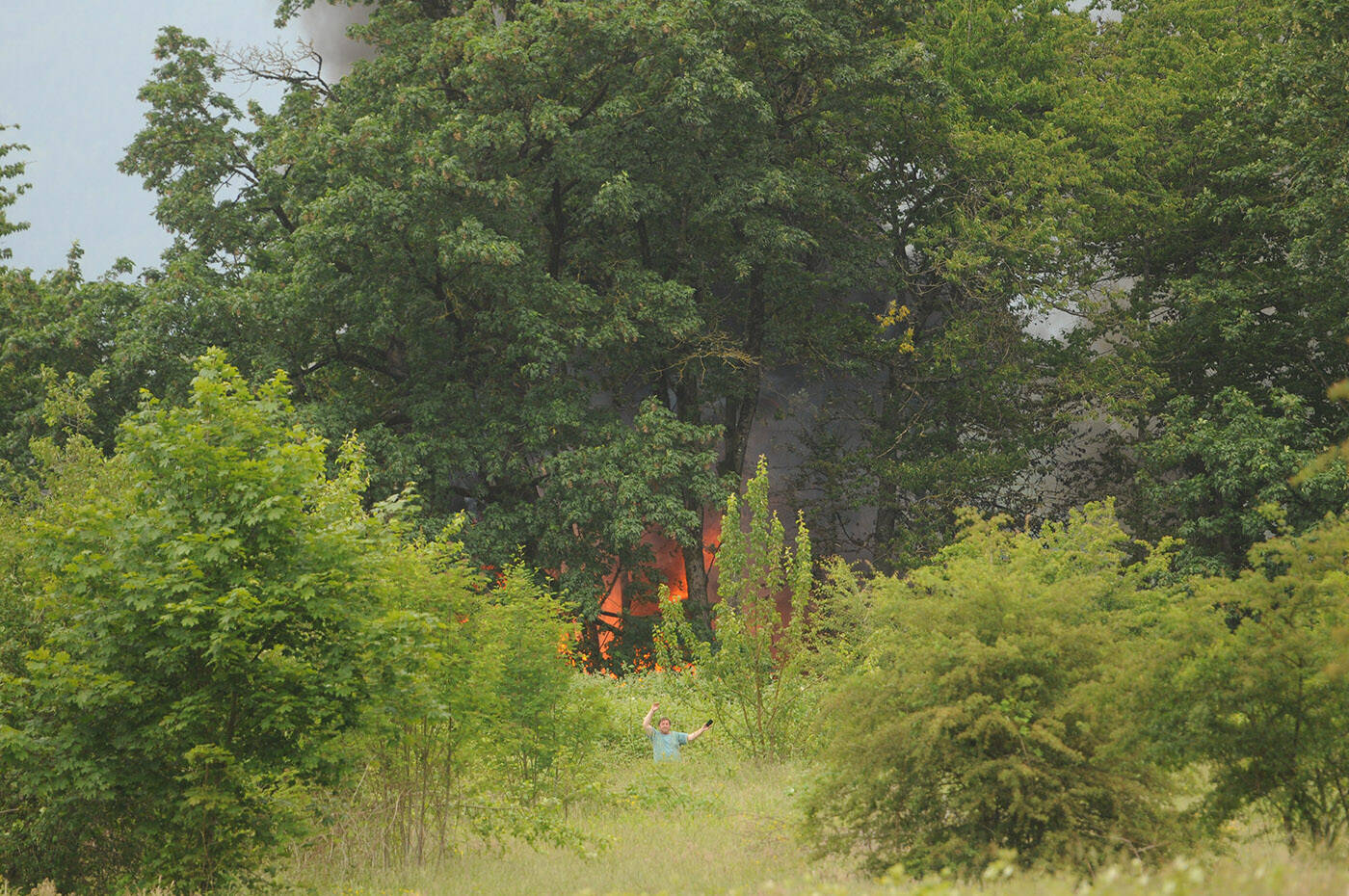 A man waves his arms to people on the dike near the west end of Marshall Avenue in Chilliwack. The Chilliwack Fire Department was called to an RV fire on Skwali reserve on Wednesday, June 15, 2022. (Jenna Hauck/ Chilliwack Progress)
