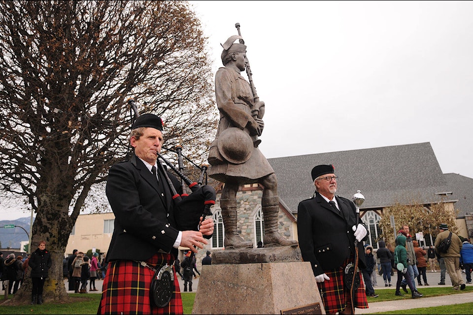 Todd Brown plays the bagpipes beside the statue of Piper James Cleland Richardson outside the Chilliwack Museum as Ken Nice looks on. The two are with the Harrison Highlanders and were part of the Remembrance Day ceremonies at Veterans’ Memorial Park on Nov. 11, 2022. (Jenna Hauck/ Chilliwack Progress file)