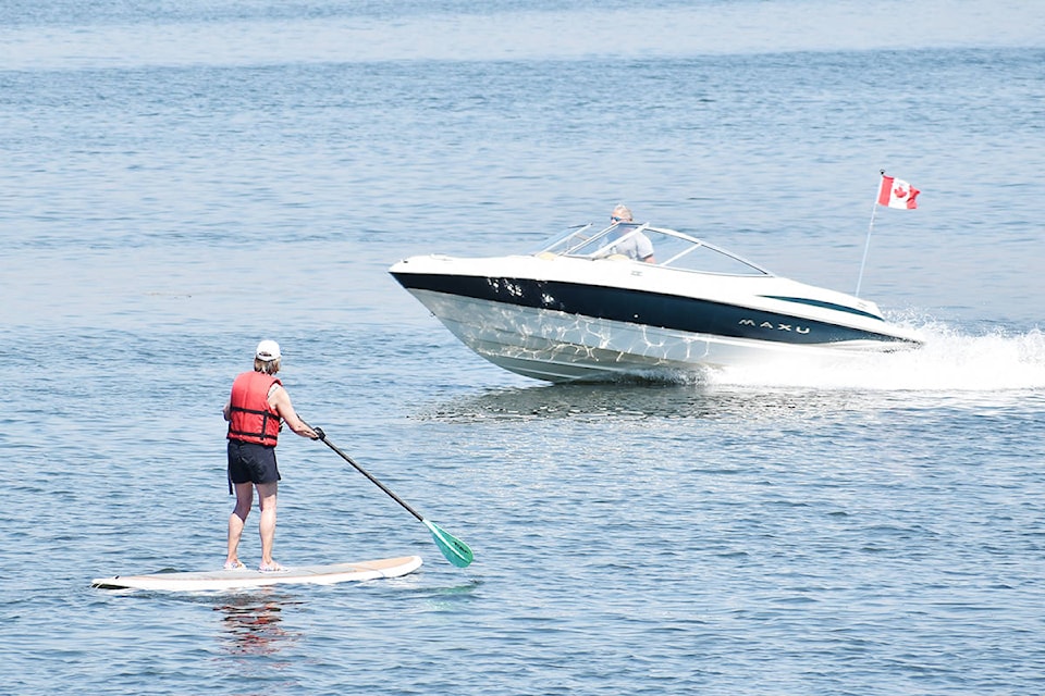 A boater cruises past a paddleboarder at Crescent Beach Monday. (Aaron Hinks photo)