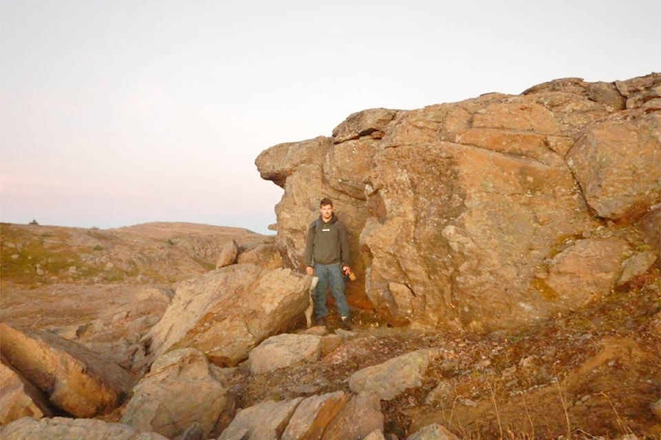 In October 2022 Josh Pettinger of Bella Coola stands next the “Huge Rock” described by Alexander Mackenzie’s journals from his journey to the Pacific Ocean in 1793. (Harvey Thommasen photo)