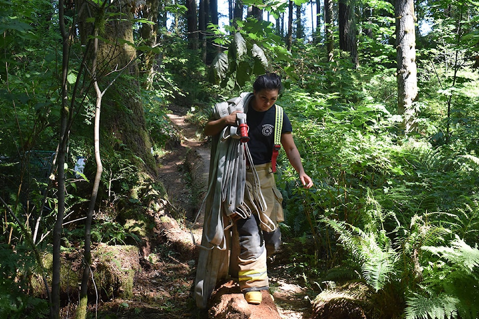 A Courtenay Fire Department member carries a hose into the heavily wooded area at Millard Nature Park in Courtenay. Photo by Terry Farrell