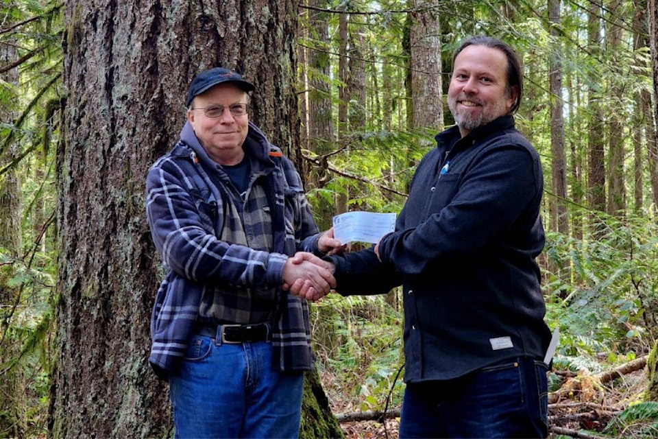 Fred Fern presents CVLT executive director Tim Ennis with a cheque. They are standing in a forest targeted for protection by the Comox Valley Land Trust. Photo by Tanis Gower