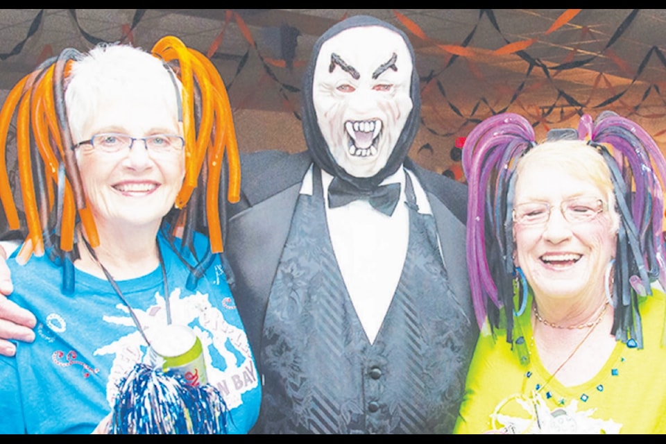 "Ann Parr (left) and Penny Repesse (right) dressed up as lighted cheerleaders. The ladies with cool hair met a stylishly dressed Dracula at the Lake Cowichan 50 Plus Activity Centre Halloween Dance Saturday evening. The dance was popular, with a final count of 52 people in attendance."
