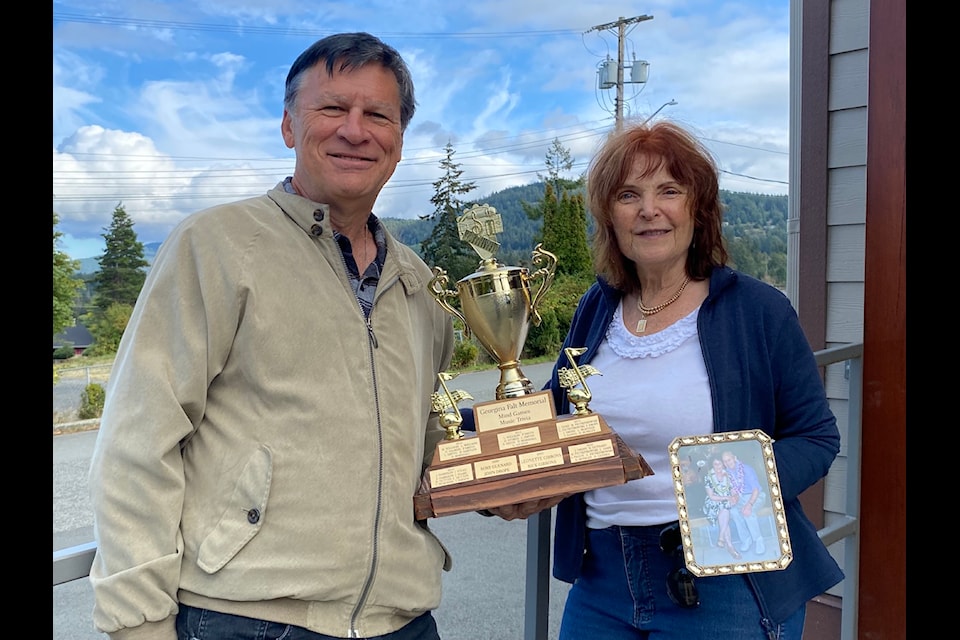 Don and Theresa Bodger stand outside the Crofton Community Centre which will be the venue  for their 12th annual Georgina Falt Memorial Mind Games Music Trivia Tournament in honour of Theresa's mom, who lived with Alzheimer's. Don holds the coveted Georgina Falt Memorial Mind Games Music Trivia trophy, while Theresa holds a photo of her mom and dad. 