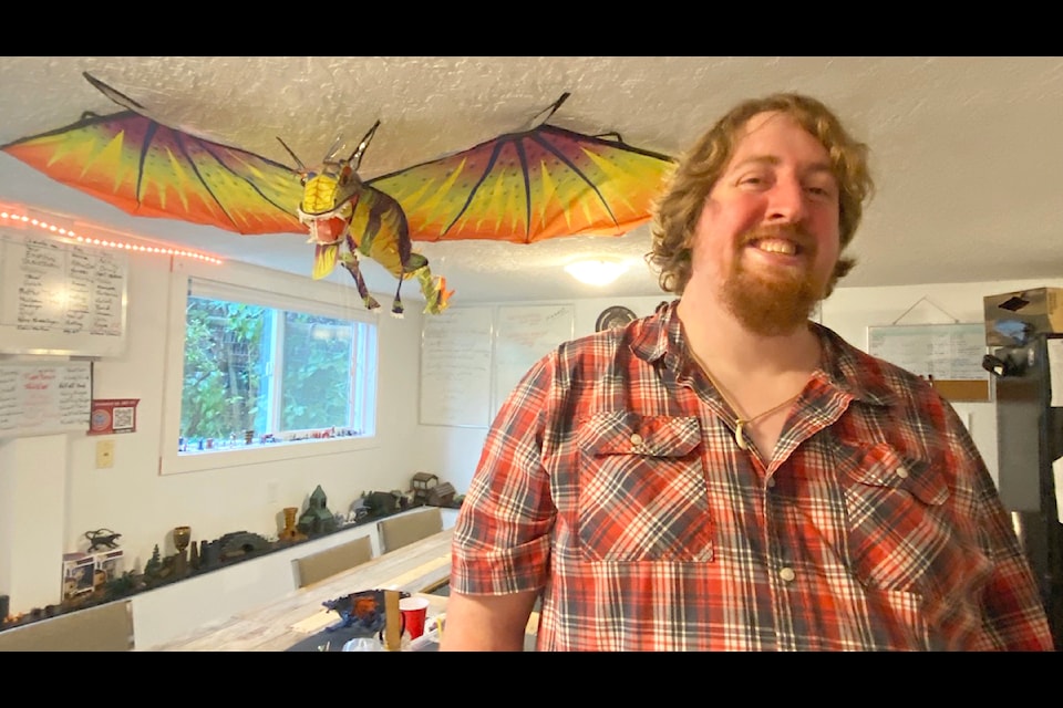 Cowichan Valley Tabletop Gaming Club founder and president Chris Lumley poses in front of the club's custom built tables where all the magic happens. Hanging above is the club's dragon mascot that they won in a raffle during their first year of existence.