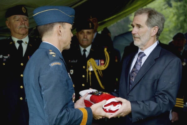 Mr. David Carey receiving the Canadian flag and medals belonging to his great-uncle Flight Sergeant John Joseph Carey. (Dept. of National Defence military history photo)