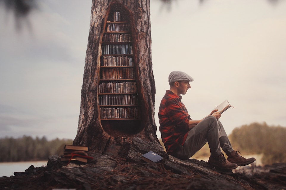 A photo taken in the Cranbrook Community Forest shows photographer Joel Robison sitting against a tree reimagined as a bookshelf (Gillian Francis/CranbrookTownsman)