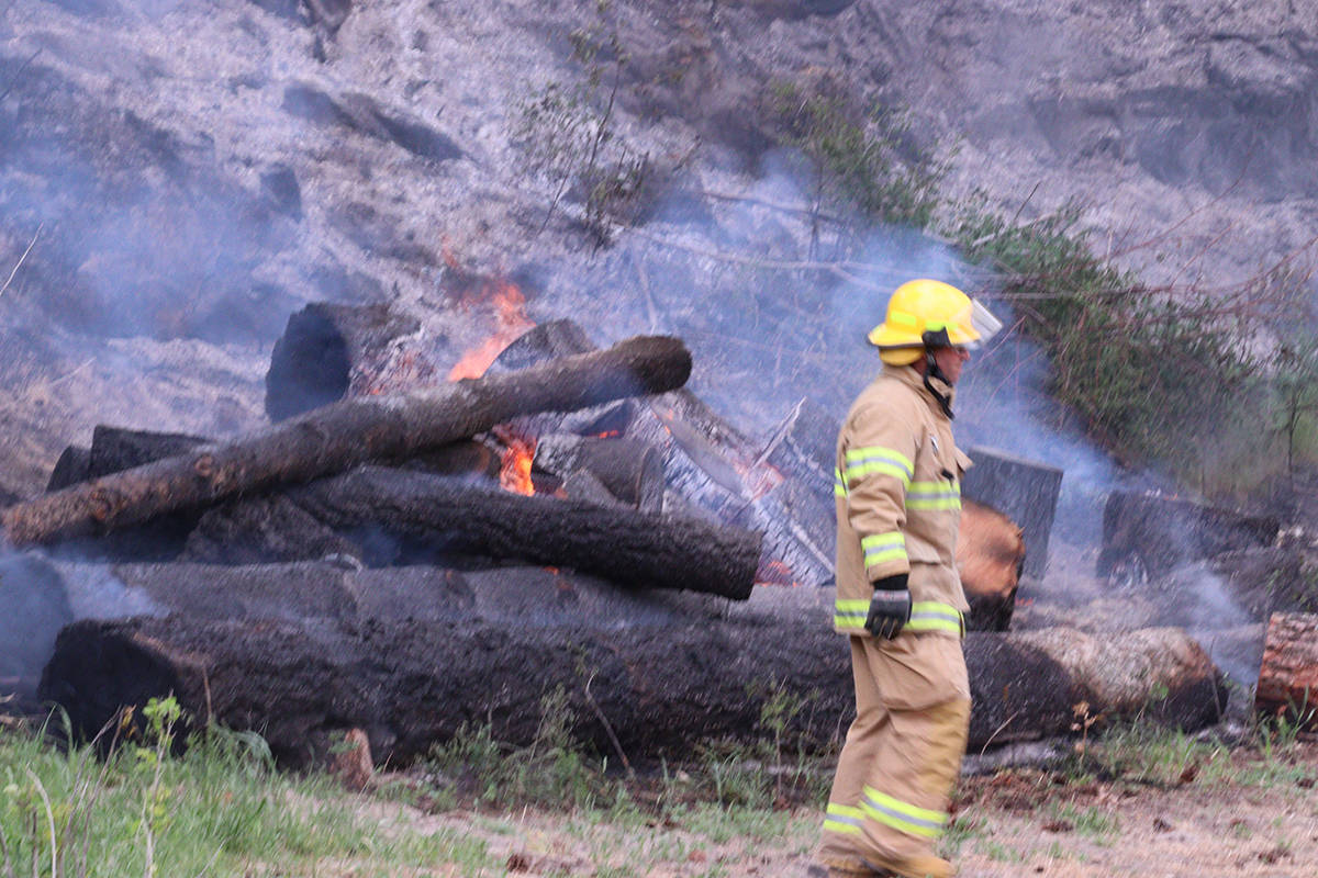 A Grand Forks Fire/Rescue volunteer stand in front of a burning log pile at the scene of Tuesdays fire, May 18. Photo: Laurie Tritschler
