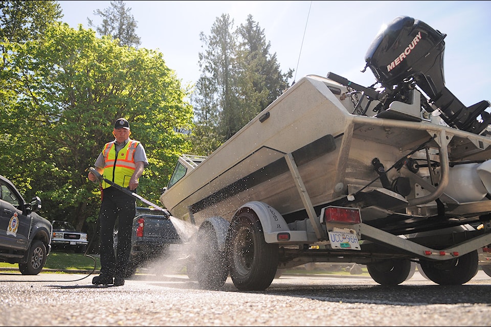 An aquatic invasive species inspector, with BC Conservation Officer Service, decontaminates a boat using hot water. 