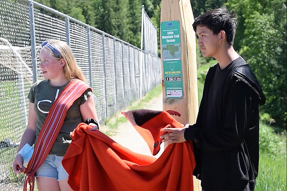 Jeremiah Vergera and Darah Thurston, Shuswap Middle School students who worked on the Trailhead posts as part of Secwépemc Landmarks Project, do the ceremonial unveiling of the first Trailhead post on June 1 near the Little Mountain fieldhouse in Salmon Arm. (Martha Wickett - Salmon Arm Observer)